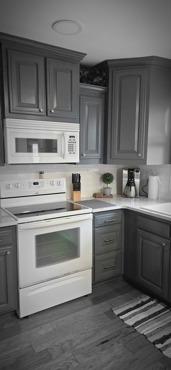 A kitchen with grey cabinets, a white microwave, a stove, and a coffee maker. - Midtown Oasis
3 Bedrooms house in Rogers with AC, private pool and more (Rogers)