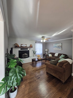 A living room with a fireplace, a ceiling fan, a brown sofa, and a coffee table. - Midtown Oasis
3 Bedrooms house in Rogers with AC, private pool and more (Rogers)