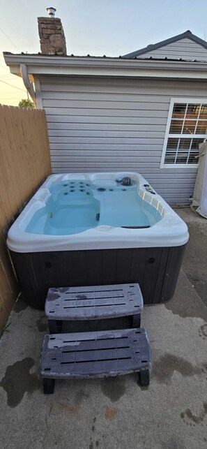 A hot tub with a wooden deck in front, a chimney on the house, and a window with blinds. - Midtown Oasis
3 Bedrooms house in Rogers with AC, private pool and more (Rogers)