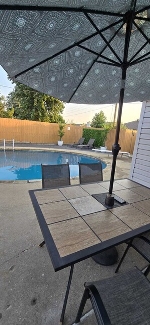 A patio with a pool, outdoor furniture, and a patterned umbrella. - Midtown Oasis
3 Bedrooms house in Rogers with AC, private pool and more (Rogers)
