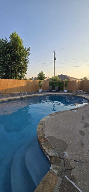 A swimming pool with a wooden fence, a metal ladder, and a paved deck. - Midtown Oasis
3 Bedrooms house in Rogers with AC, private pool and more (Rogers)
