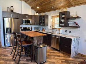 A modern kitchen with dark cabinets, stainless steel appliances, a wooden island, and a herringbone-patterned floor. - New! Spacious Bobcat lodge w/Hot Tub, Starlink (Fairplay)