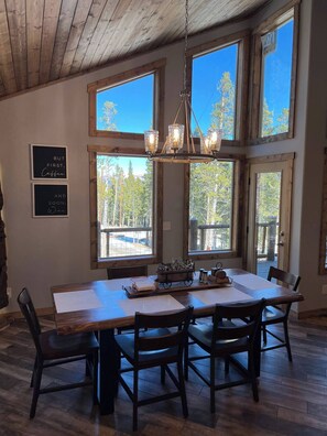 A dining area with a large wooden table, six chairs, and a chandelier. - New! Spacious Bobcat lodge w/Hot Tub, Starlink (Fairplay)