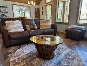 A cozy living room with a brown leather sofa, a wooden coffee table, and a patterned rug. - New! Spacious Bobcat lodge w/Hot Tub, Starlink (Fairplay)