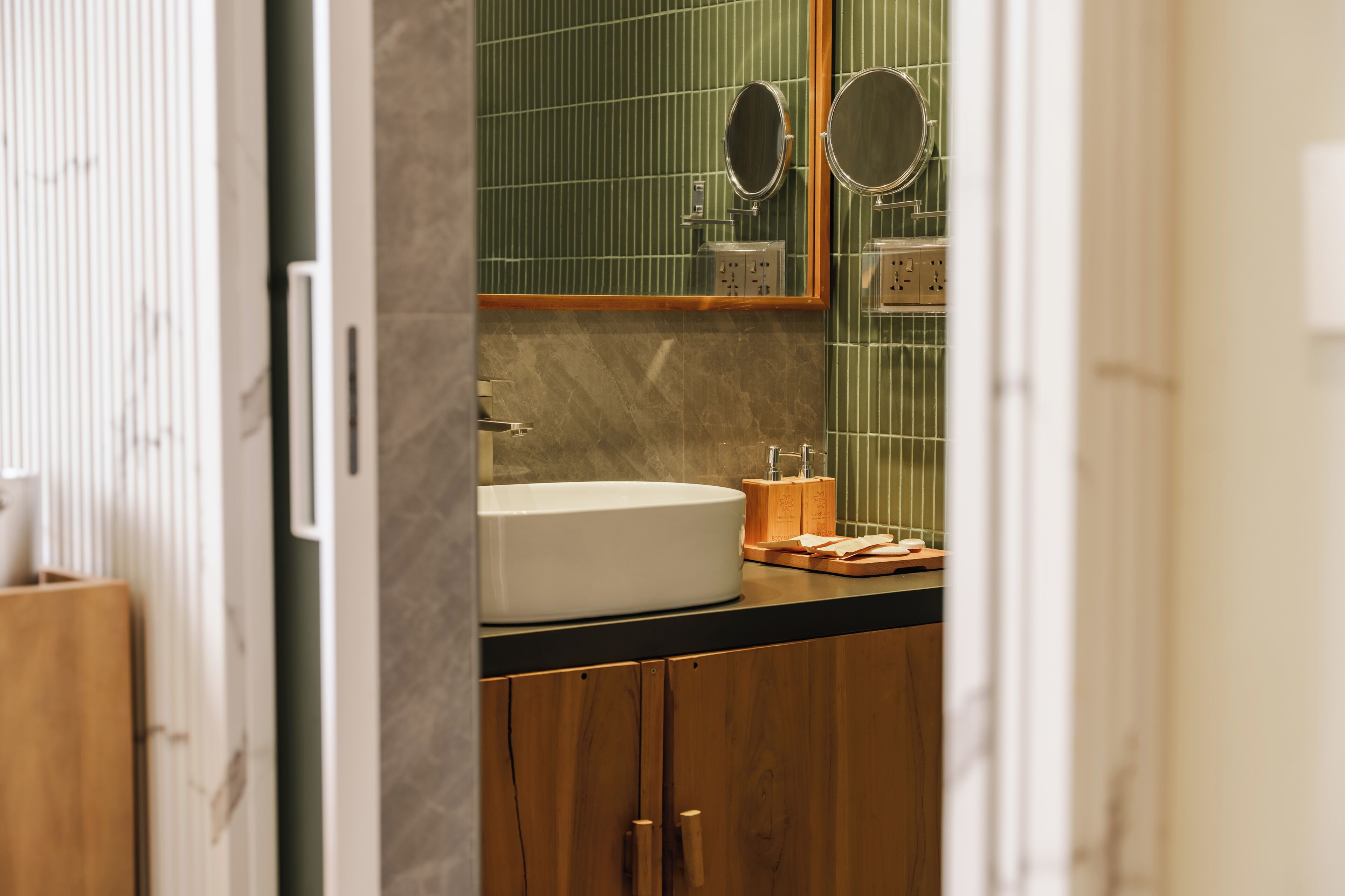 Ein Badezimmer mit einem weißen Waschbecken, Holzschränken und einer grün gefliesten Wand.