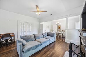 Ein Wohnzimmer mit einer Couch, Deckenventilator, einem Essbereich mit Stühlen und einem Kamin.