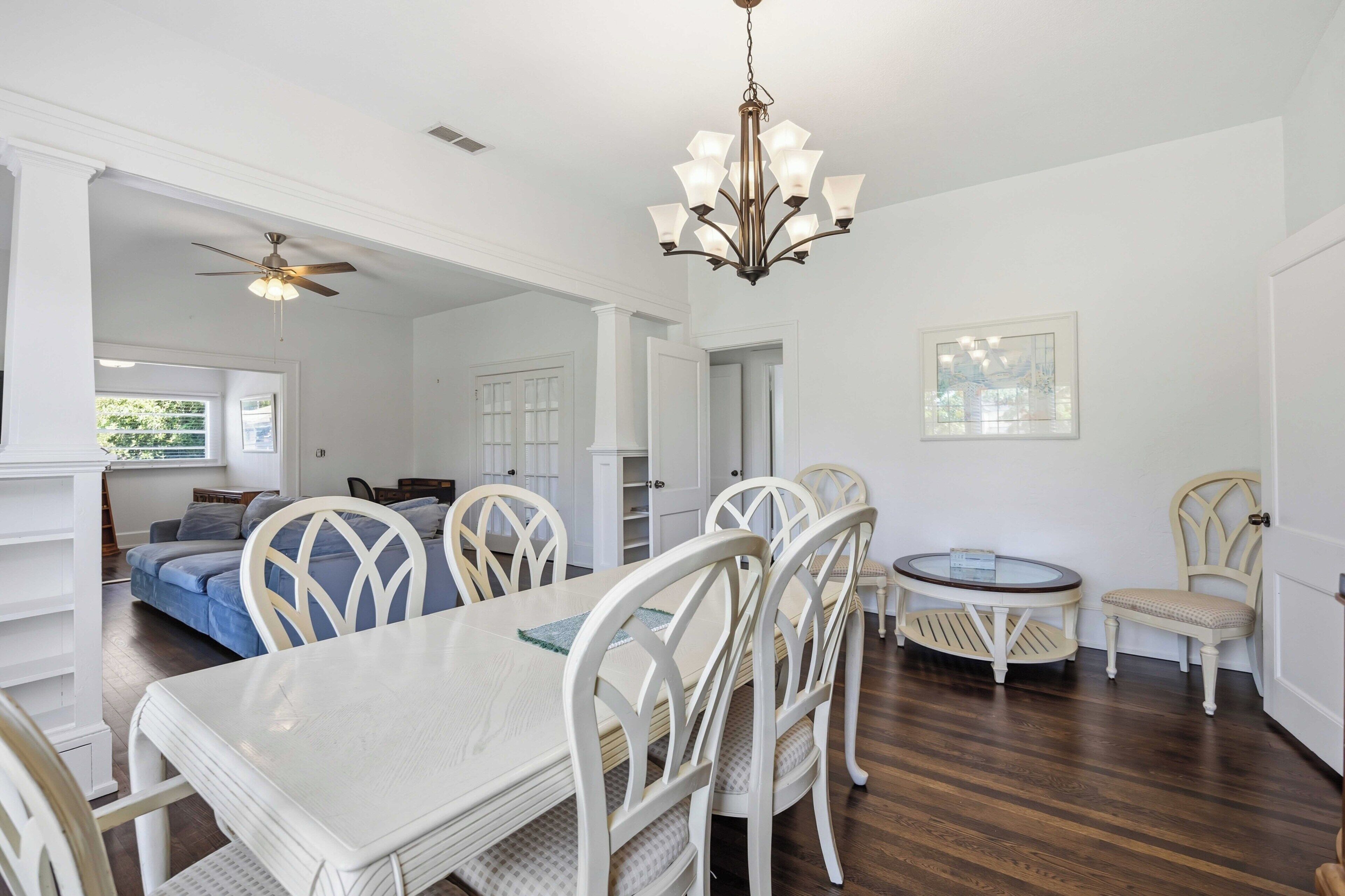 A dining area with a white table and chairs, a chandelier, and a ceiling fan.