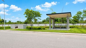 A covered bus stop with a bench, a concrete wall, and greenery in the background.