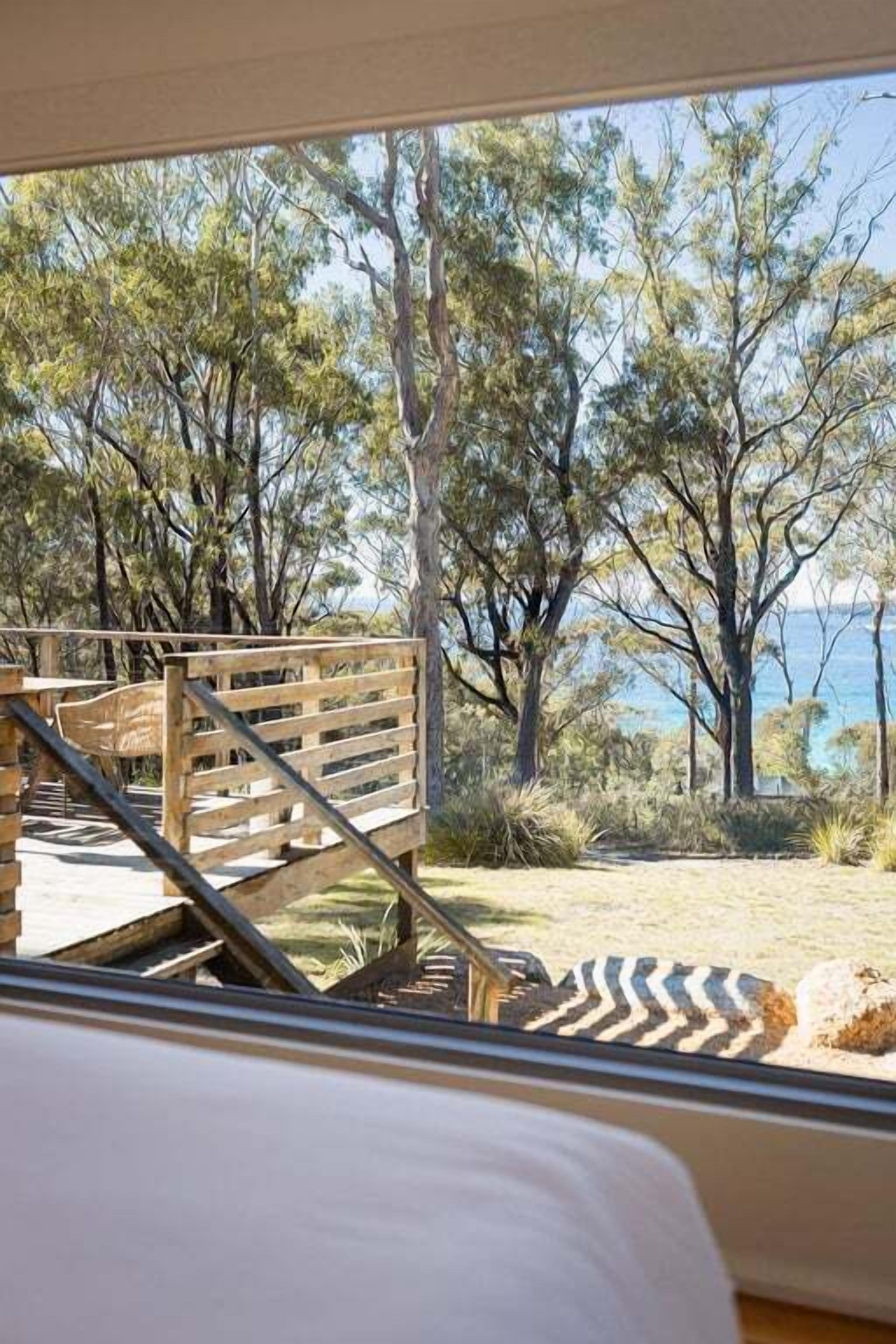 A wooden deck leading to a beach with trees and a view of the sea.
