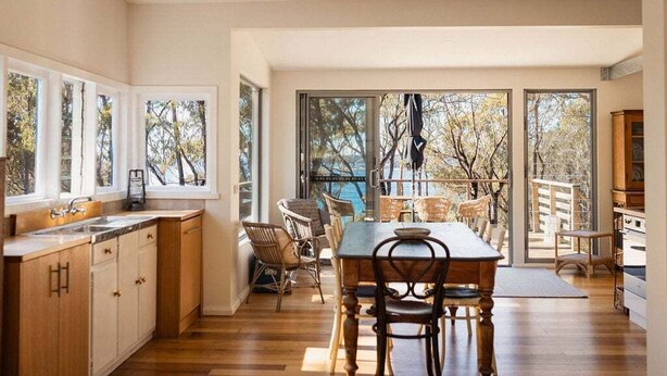 Une cuisine moderne avec de grandes fenêtres, un coin repas avec des meubles en osier et une vue sur les arbres.