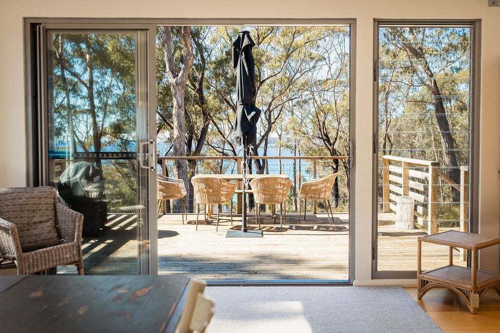 A room with a large sliding glass door leading to an outdoor deck with wicker furniture and a view of trees and water.