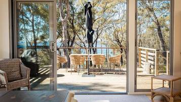 A room with a large sliding glass door leading to an outdoor deck with wicker furniture and a view of trees and water.