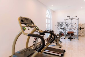 Un gimnasio con cintas de correr, un banco de pesas y una máquina de ejercicios fijada a la pared.
