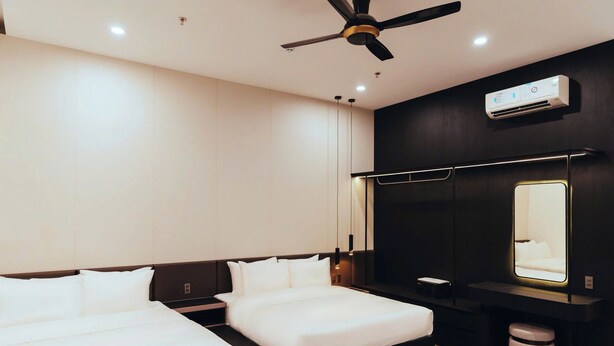 Habitació d'hotel moderna amb llit, taules de nit, ventilador de sostre, aire condicionat, un mirall gran i un petit cub de basures.