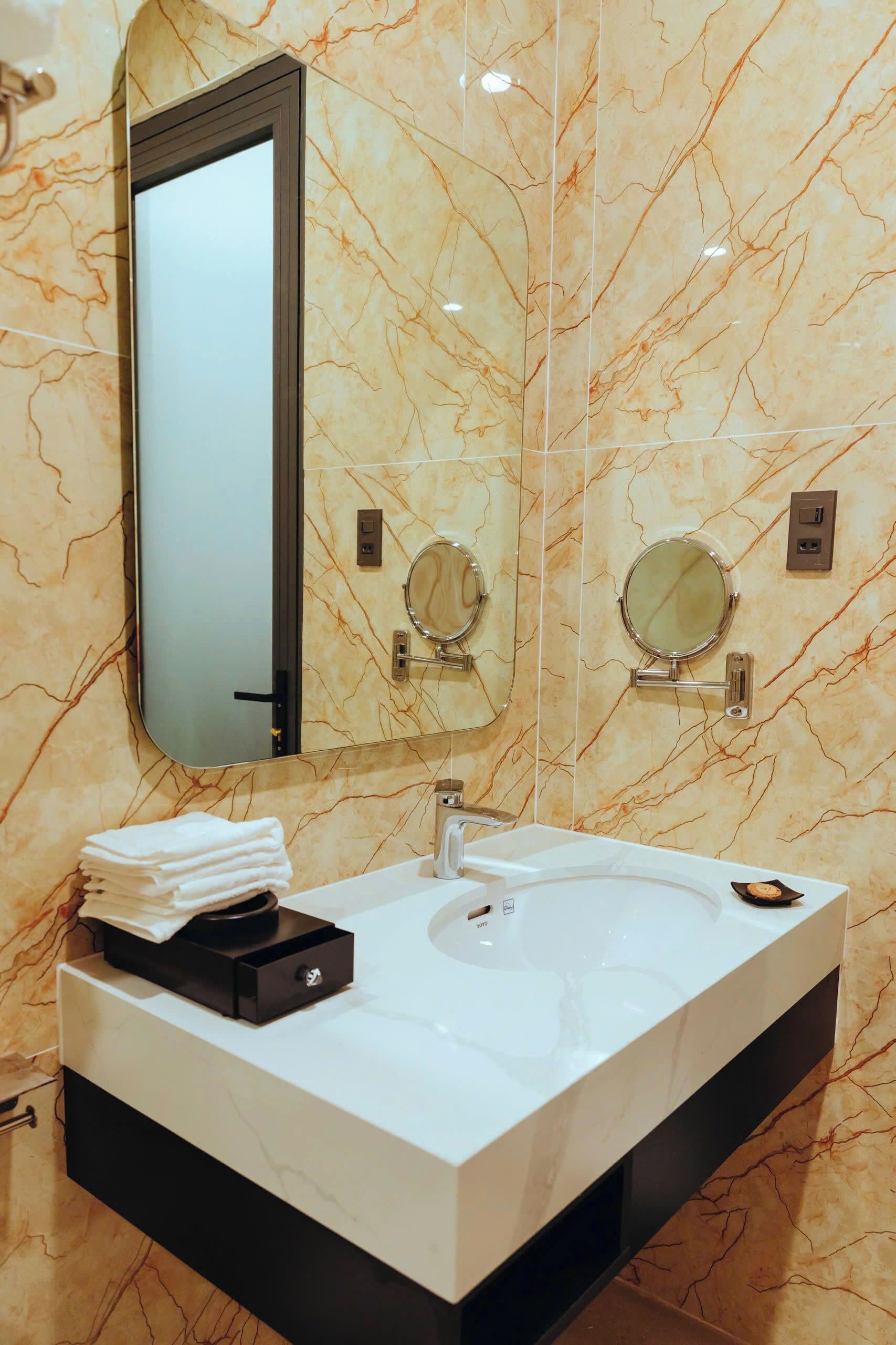 A bathroom with a marble vanity, a large mirror, two round mirrors, a sink, and a towel dispenser.