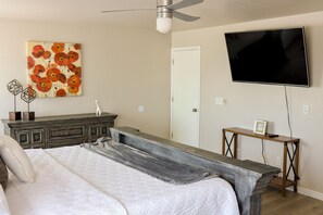 A bedroom with a bed, a dresser, a TV, and a painting on the wall.