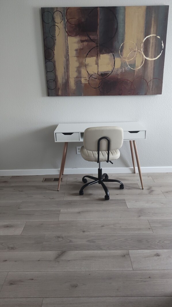 Un espacio de oficina moderno con un escritorio blanco, una silla de cuero y un cuadro abstracto grande en la pared.