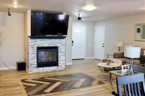 A living room with a fireplace, a flat-screen TV, a round coffee table, and a sofa. - Cozy Home on the Lake in Denver (Thornton)