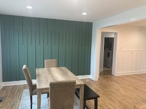 Ein Essbereich mit Holztisch und -stühlen, einer Wand in Türkis und einem Waschraum im Hintergrund.