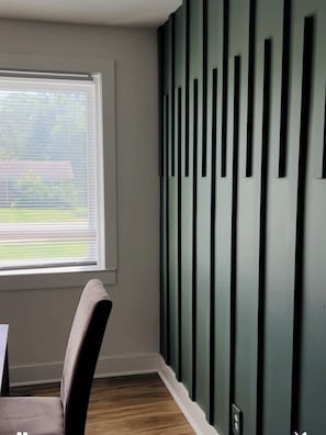 Ein Zimmer mit Fenster, einem Sessel und einer Wand mit vertikalen schwarzen Paneelen.