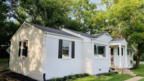 Ein weißes Einfamilienhaus mit Veranda, kleinem Garten und einem Weg zum Eingang.