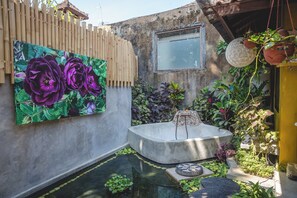 Ein Innenhof mit einer Betonbadewanne, einem Holzzaun und einem großen Gemälde lila Blumen.