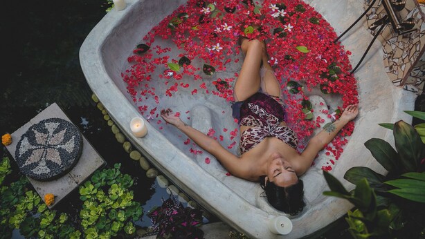 A person relaxing in a stone bathtub filled with water and red flowers, surrounded by greenery. - 1BR in the heart of Ubud - Tiny Bali (Ubud)