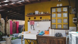 A kitchen with a white sink, wooden cabinets, a yellow wall, and a window with frosted glass. - 1BR in the heart of Ubud - Tiny Bali (Ubud)