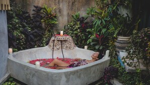 A person relaxing in a concrete bathtub filled with water and rose petals, surrounded by lush greenery and potted plants. - 1BR in the heart of Ubud - Tiny Bali (Ubud)