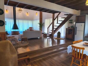 A spacious living area with a wooden staircase, a dining table, and a kitchen area. - Country house in Lages, Aconchego Serrano, with outdoor hot tub. (Lages)