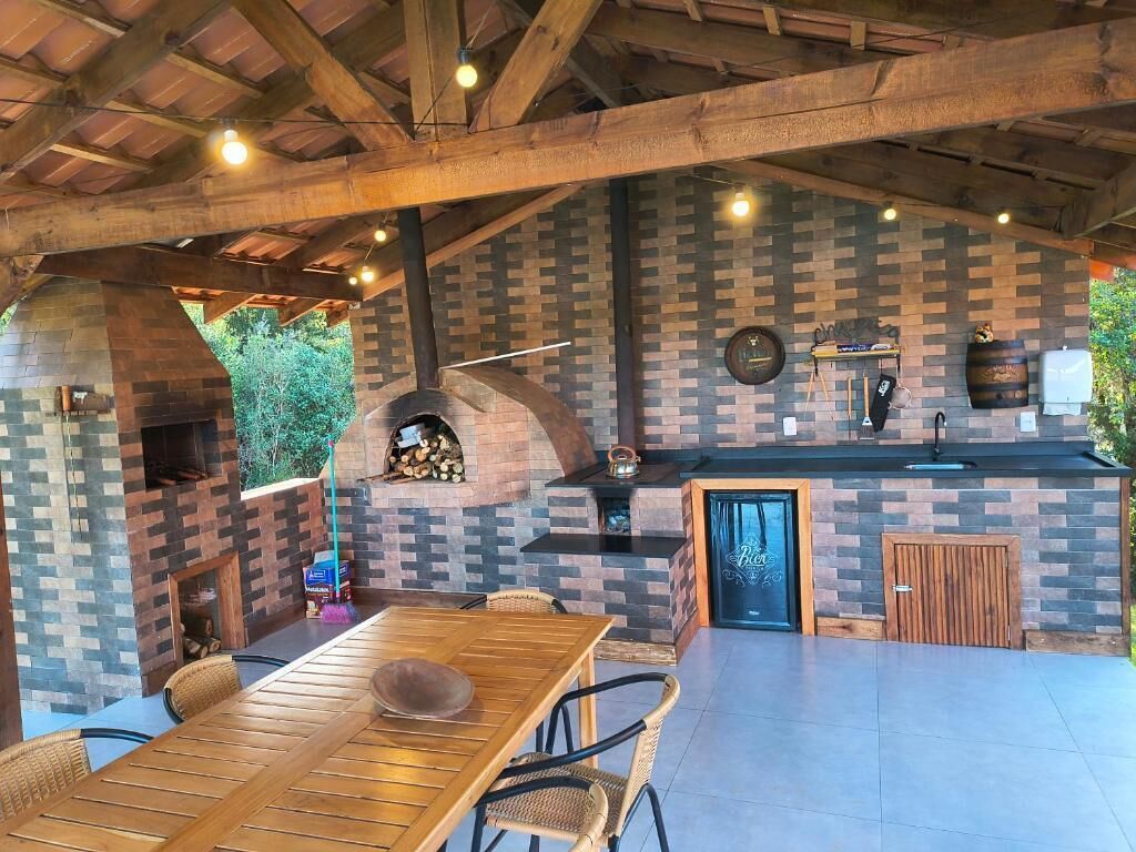 Een buitenkeuken met een bakstenen muur, houten balken en een eethoek met een tafel en stoelen.