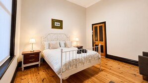 Una camera da letto con un letto, comodini, una ventola a soffitto, una porta in legno e un quadro appeso al muro.