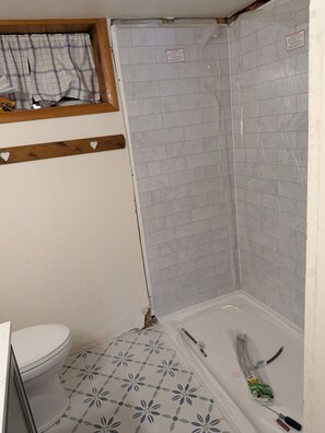 Une salle de bain avec douche, toilettes et carrelage au sol à motifs.