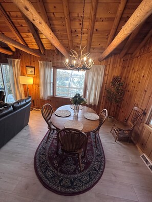 Ein Holzinterieur mit einem runden Esstisch, Stühlen, einer Chandelüster und einem Sofa.