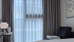 Een hotelkamer met een bed, een stoel, een bureau met een lamp en een raam met gordijnen.