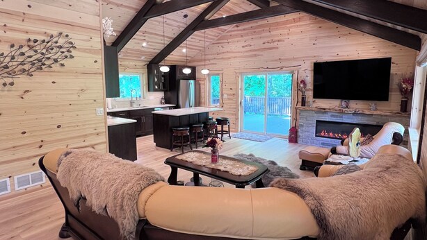 Un interior de cabaña acogedor, con un sofá, chimenea, televisor y una zona de cocina.