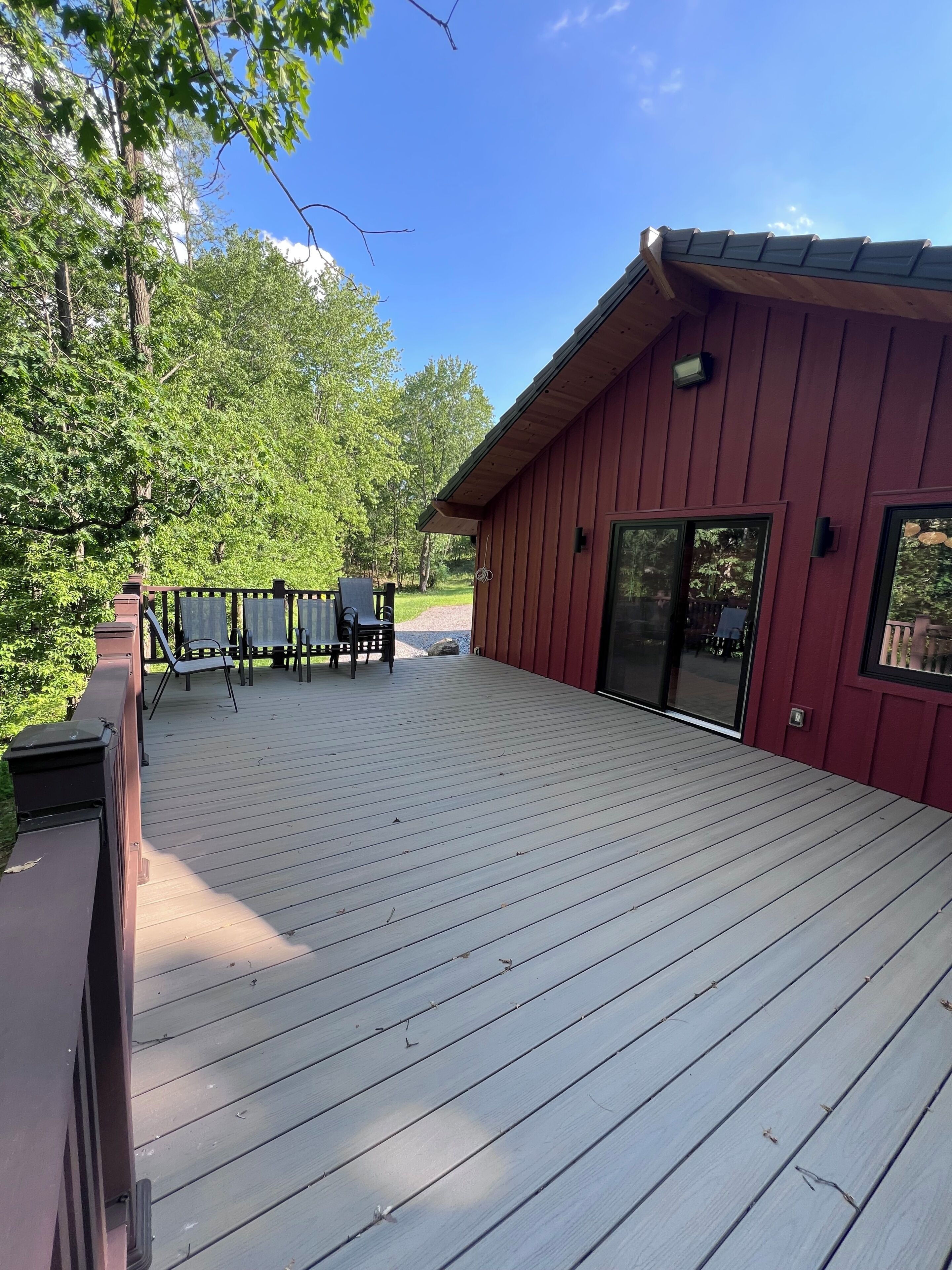 A wooden deck with outdoor furniture, a building with a red exterior, and a clear blue sky.