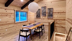Un interior de madera con una larga mesa, sillas y una lámpara colgante.