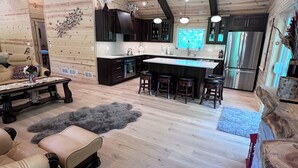 Amplia sala de estar con un techo de madera grande, una isla central con taburetes, armarios de madera oscura y vistas al área de la cocina.