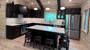 Una cocina moderna con una isla grande, armarios oscuros, electrodomésticos de acero inoxidable y techo de madera.
