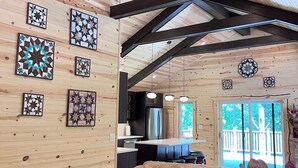 Interior acogedor de una cabaña con techo de madera, un sofá con un perro, una zona de cocina y decoración en las paredes.