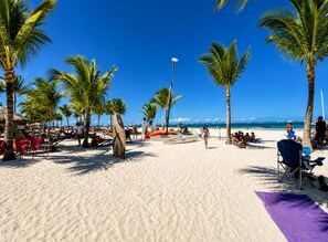 A beach with palm trees, a surfboard, and beach chairs. - Aura:Wonderful 1-bedroom apartment with AC in sunny Punta Cana (Punta Cana)
