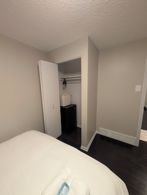 Ein Hotelzimmer mit einem Bett, einem kleinen Schrank, einer weißen Wand und einem dunklen Boden.