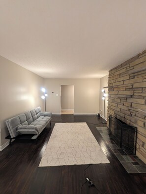 A living room with a sofa, a patterned rug, a stone fireplace, and two floor lamps. - Private Room with Shared Bathroom Near Mooney's Bay (Ottawa)