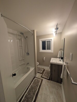 Een badkamer met een bad, douche, toilet, wastafel en een raam.