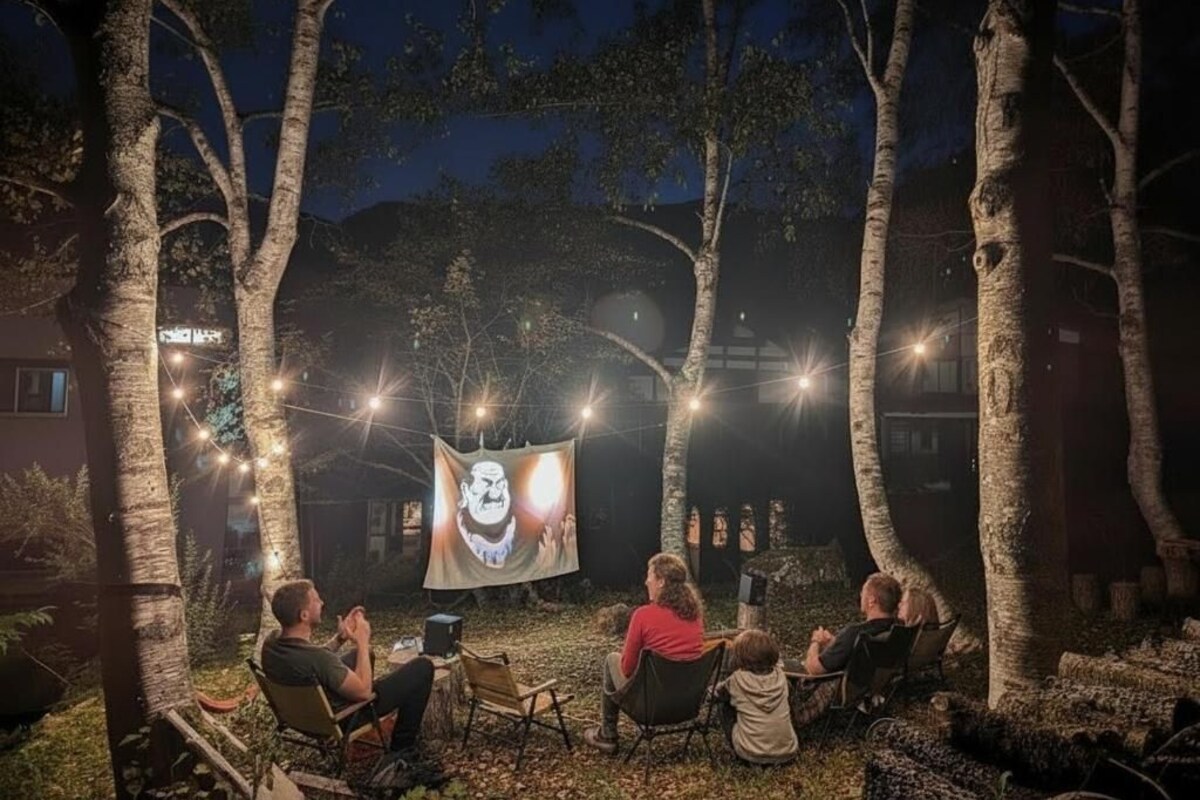 Nit de cinema a l'aire lliure, amb una gran pantalla, persones assegudes en cadires i llums penjades.