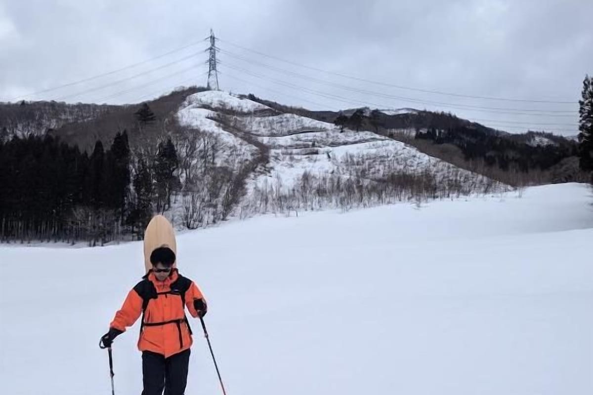 Eine Person fährt auf einem verschneiten Hang Ski, im Hintergrund ist ein Strommasten zu sehen.