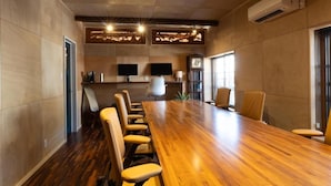 Une salle de conférence avec une longue table en bois, des fauteuils en cuir, un téléviseur à écran plat et une horloge au mur.