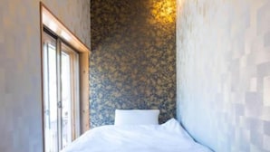 Une petite pièce avec un lit, une fenêtre et un mur à la texture particulière.