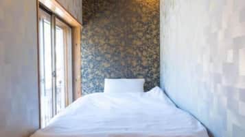 A narrow room with a bed, a window, and a textured wall.